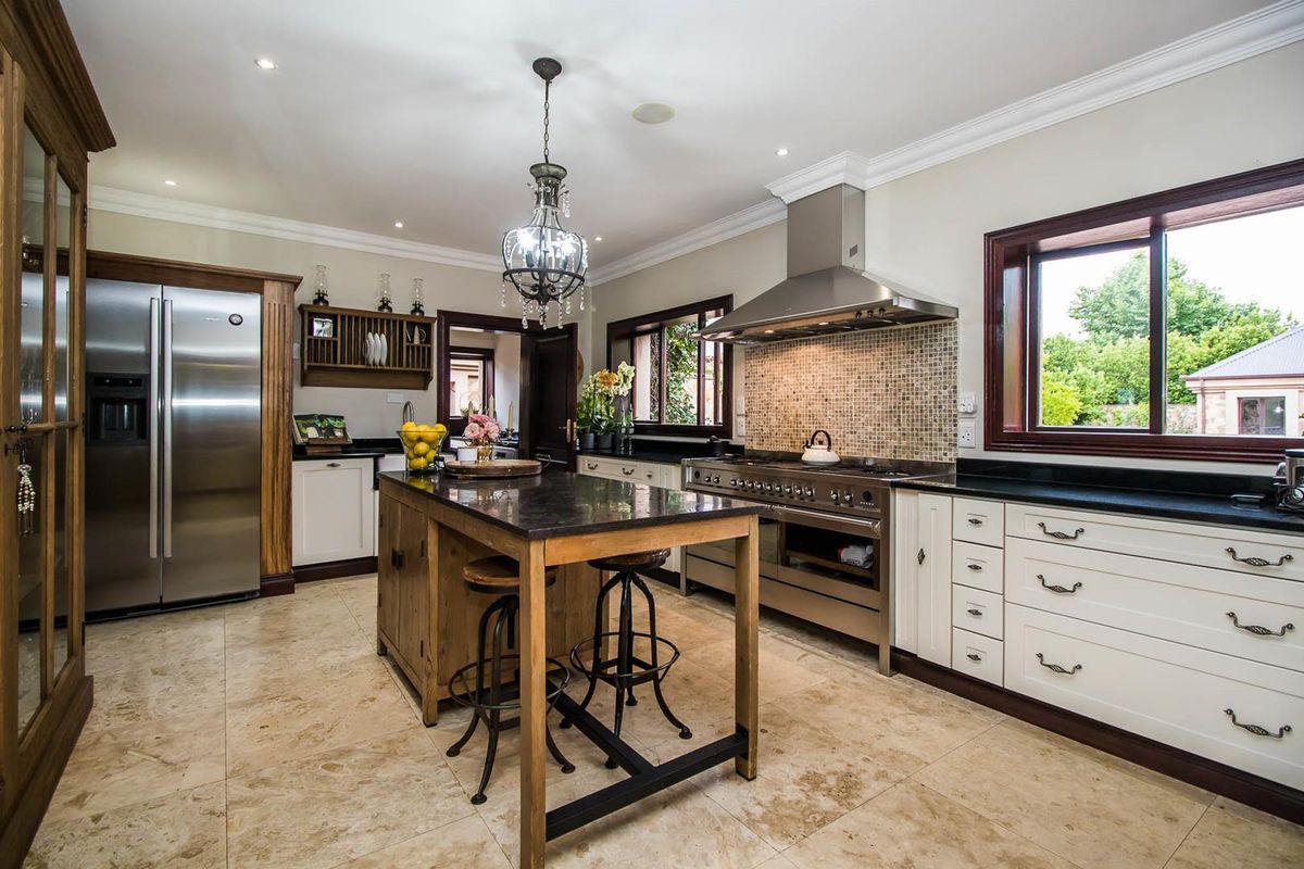 Spacious kitchen featuring a central island, stainless steel gas range with extractor hood, stone countertops, and tiled flooring.