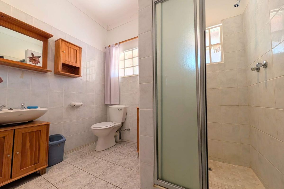 A functional bathroom featuring a shower enclosure, toilet, and wooden vanity cabinet with a basin, finished with neutral wall and floor tiles.
