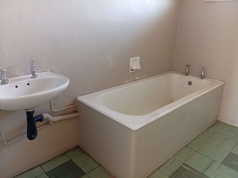 A dated bathroom featuring a built-in bathtub, pedestal basin, and tiled flooring, requiring cosmetic updates to improve its overall condition and appeal.