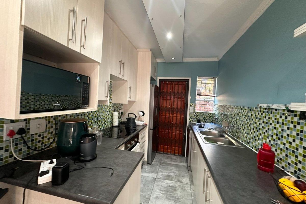 Functional kitchen featuring light-toned cabinetry, dark laminate countertops, mosaic tile backsplash, and integrated appliances with a rear security door access.