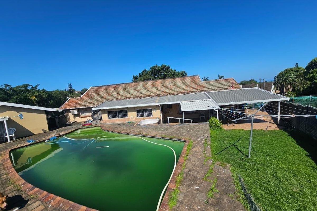 Rear exterior view of the property featuring a swimming pool, paved patio area, and covered outdoor space with a tiled roof.