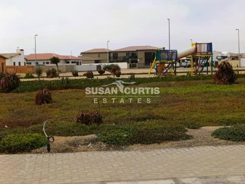 A communal outdoor garden area featuring a playground structure, paved pathways, and established landscaping within a residential estate setting.