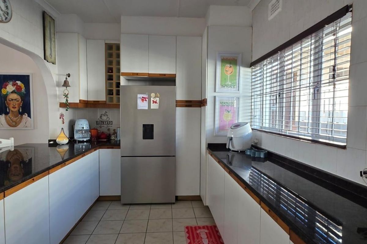 A functional kitchen featuring white cabinetry, dark granite countertops, tiled flooring, and a large window with blinds.