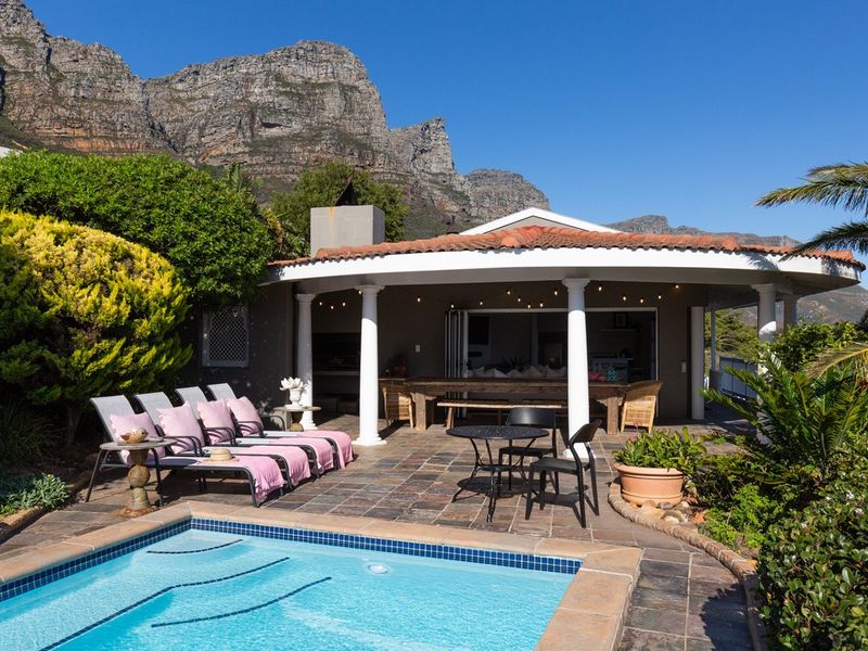 Outdoor pool area featuring a covered patio with built-in braai, tiled flooring, and scenic mountain views.