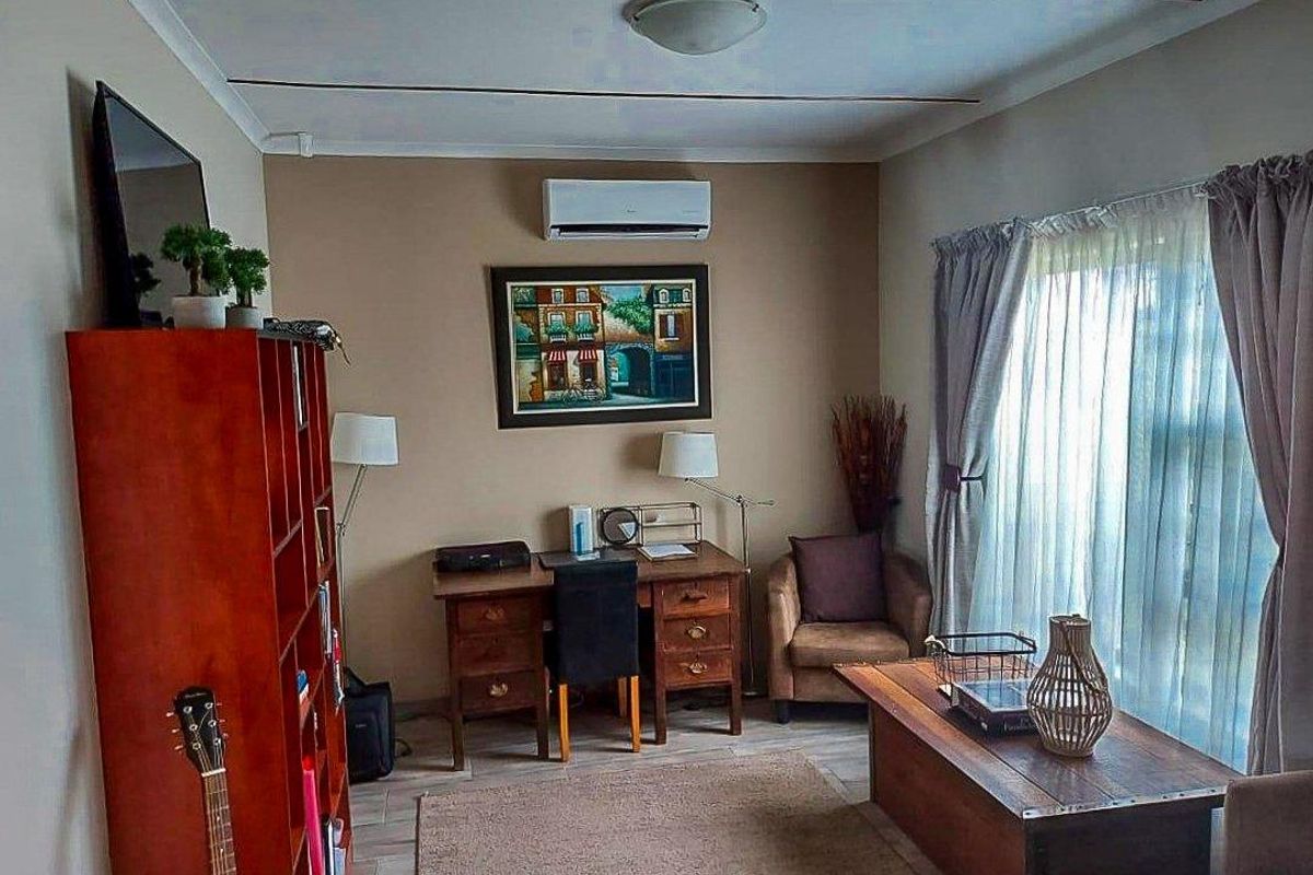 A comfortable living room featuring a wall-mounted air conditioning unit, tiled flooring, and large windows allowing for natural light.