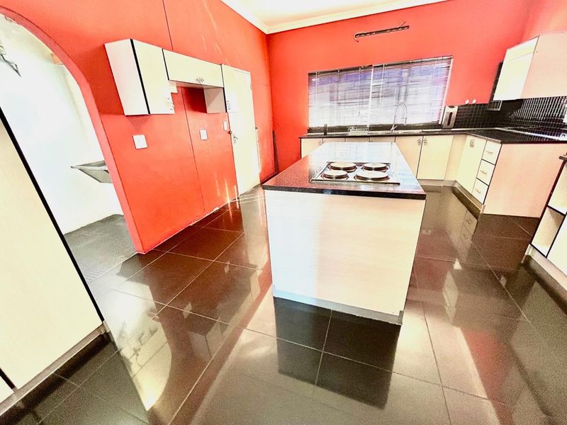 Spacious kitchen featuring a central island with a built-in hob, granite countertops, and ample cabinetry, finished with dark tiled flooring.