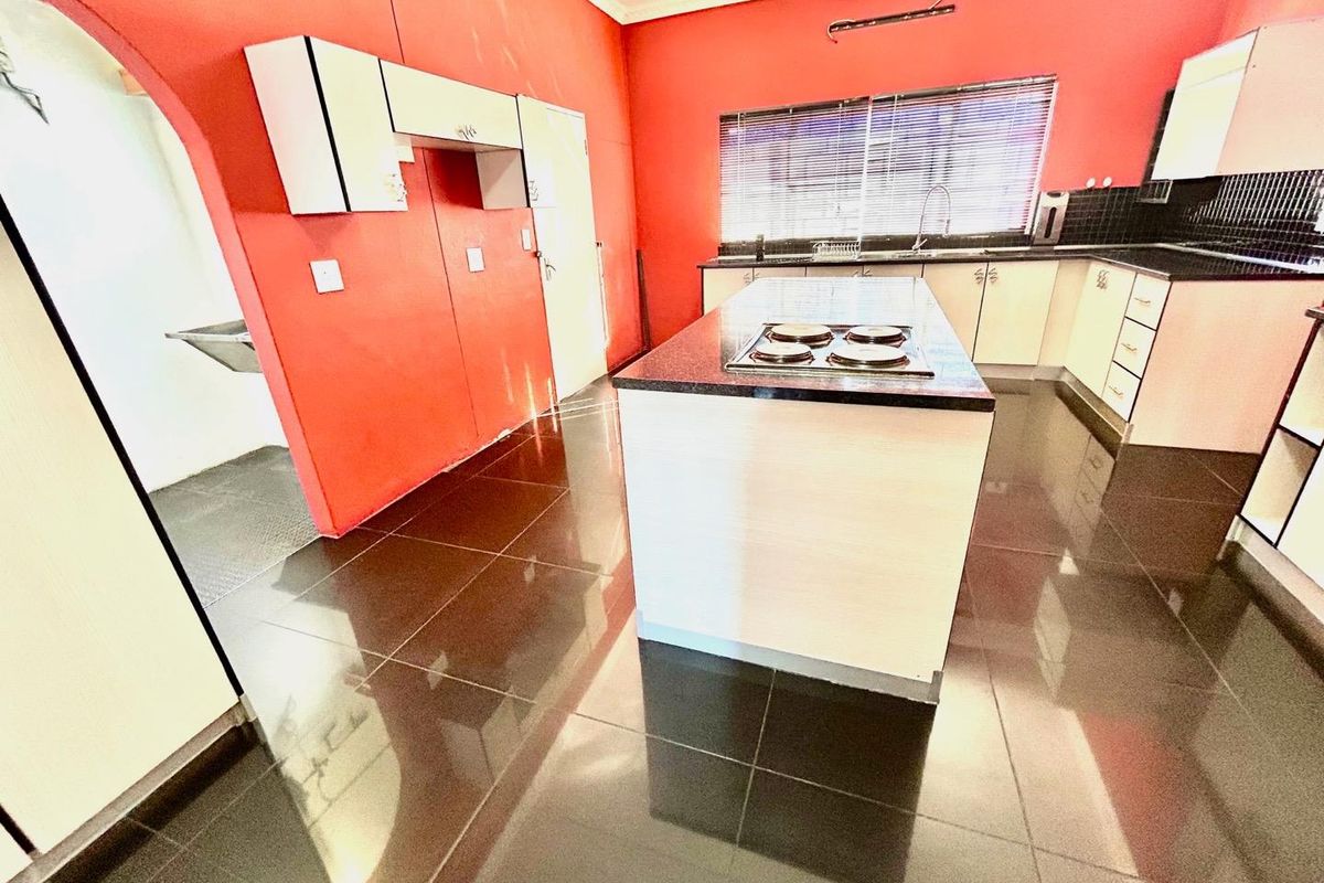 Spacious kitchen featuring a central island with a built-in hob, granite countertops, and ample cabinetry, finished with dark tiled flooring.