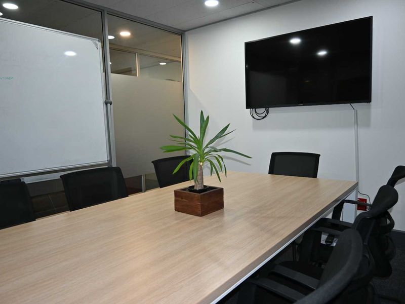 A professional office meeting room featuring a glass partition wall, recessed lighting, and a wall-mounted television for presentations.