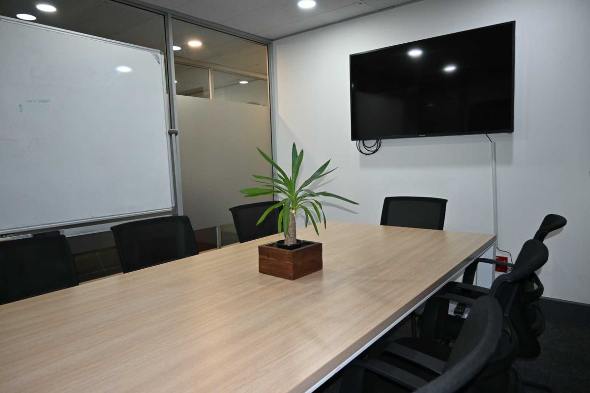 A professional office meeting room featuring a glass partition wall, recessed lighting, and a wall-mounted television for presentations.