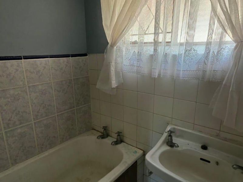 A dated bathroom featuring a standard bathtub, pedestal basin, and ceramic wall tiling, requiring modernization to improve its aesthetic appeal.