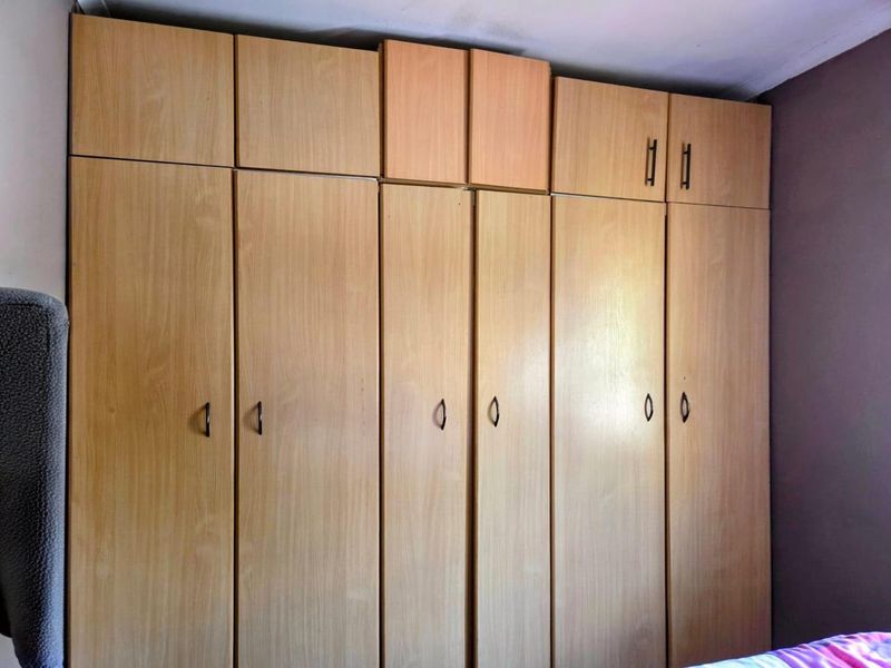 A bedroom featuring floor-to-ceiling light wood built-in cupboards providing ample storage space.
