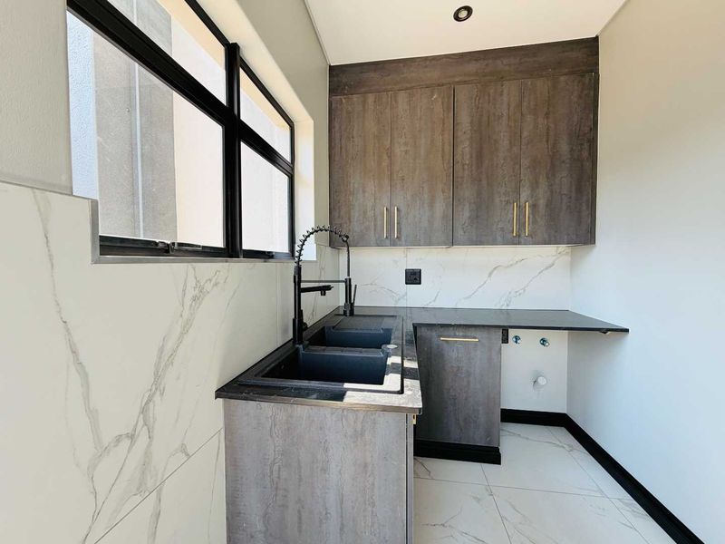 Modern scullery featuring dark wood-look cabinetry, marble-effect wall tiles, a double sink with a black gooseneck faucet, and plumbing connections for appliances.