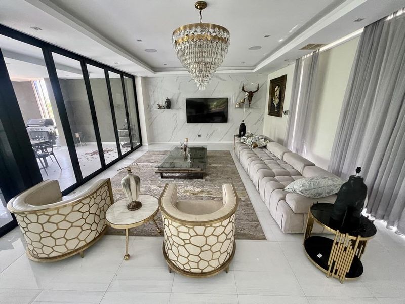 Spacious, modern living room featuring a marble-look feature wall, recessed lighting, a crystal chandelier, and large sliding glass doors opening to the patio.