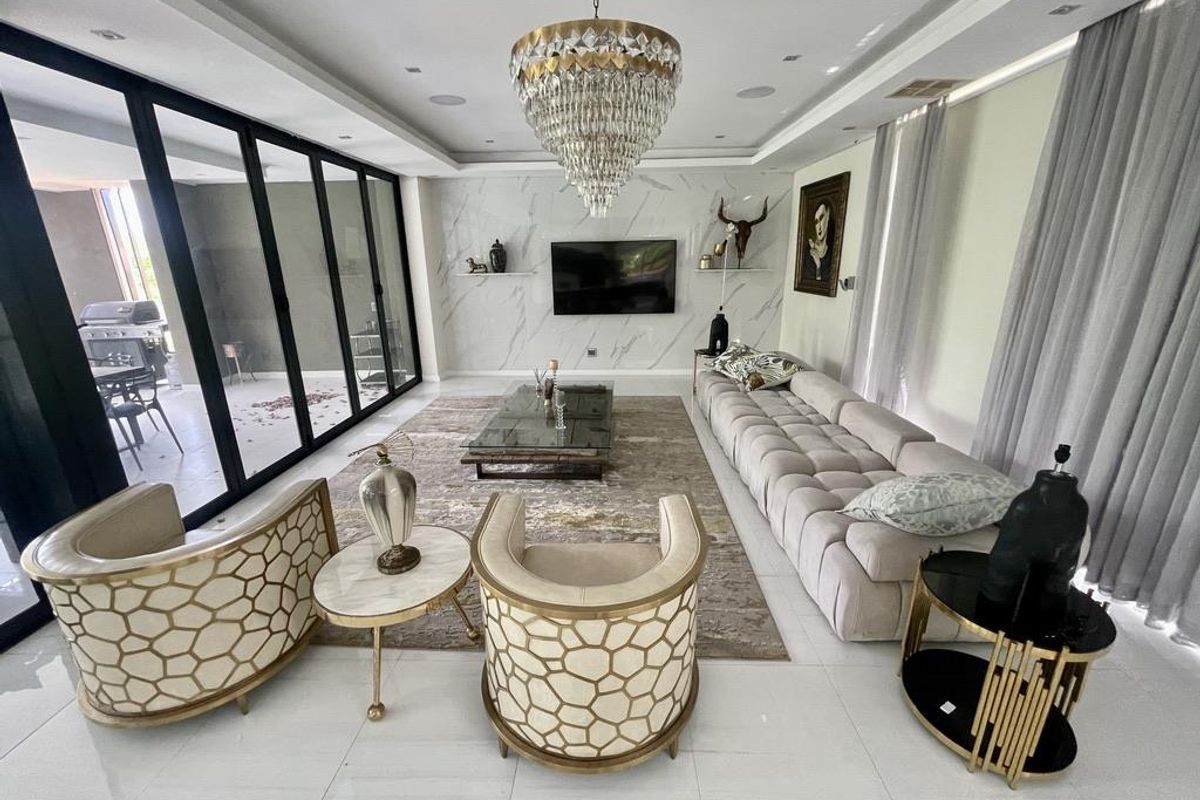 Spacious, modern living room featuring a marble-look feature wall, recessed lighting, a crystal chandelier, and large sliding glass doors opening to the patio.