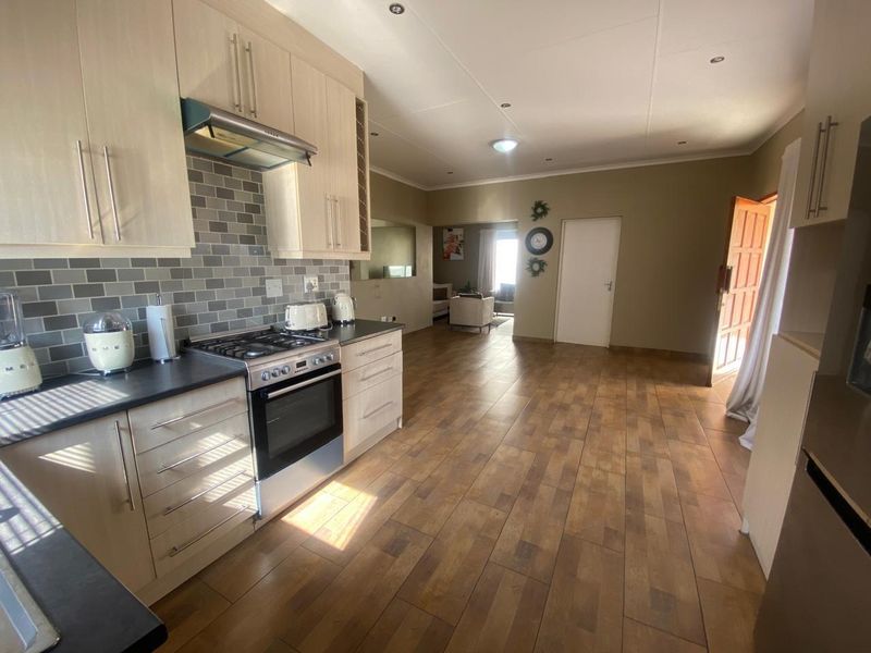 Open-plan kitchen and living area featuring light wood cabinetry, gas hob, electric oven, and modern tiled backsplash with durable wood-look flooring.