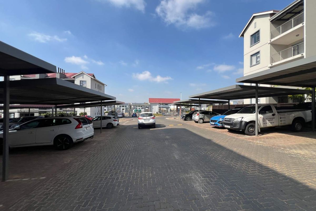 Outdoor parking area featuring covered carports with paved surfacing, situated within an apartment complex.