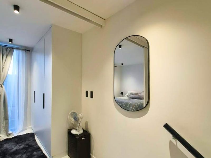 A modern hallway featuring built-in storage cupboards, recessed ceiling lighting, and a staircase handrail, leading towards a bedroom area.