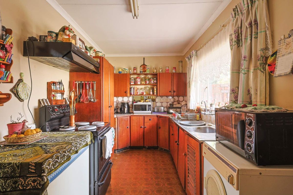 A dated kitchen featuring traditional wooden cabinetry, a double bowl stainless steel sink, and a tiled splashback, offering significant potential for modern renovation.