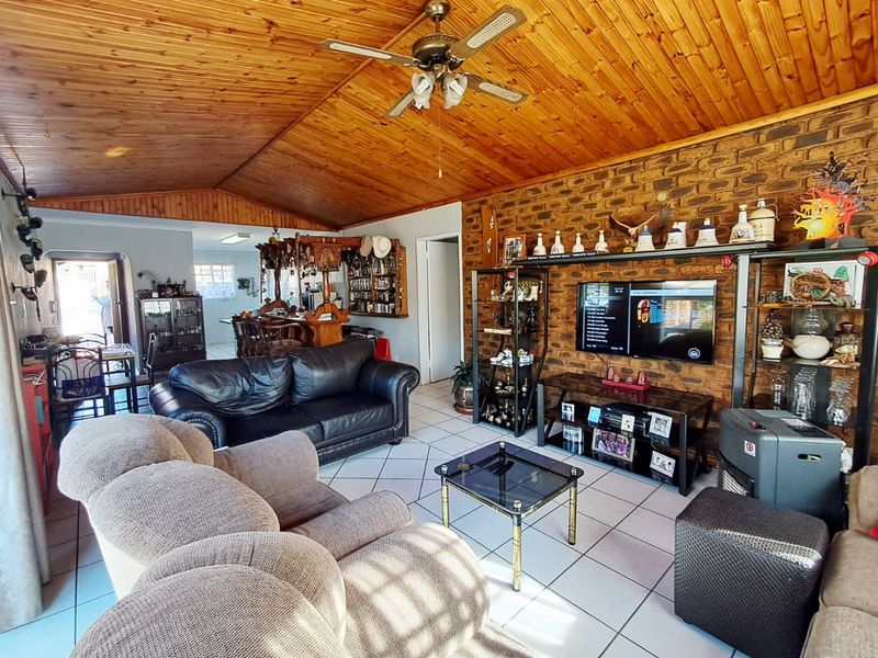 Open-plan living area featuring an exposed timber vaulted ceiling, exposed brick feature wall, and tiled flooring, connecting to a kitchen area.