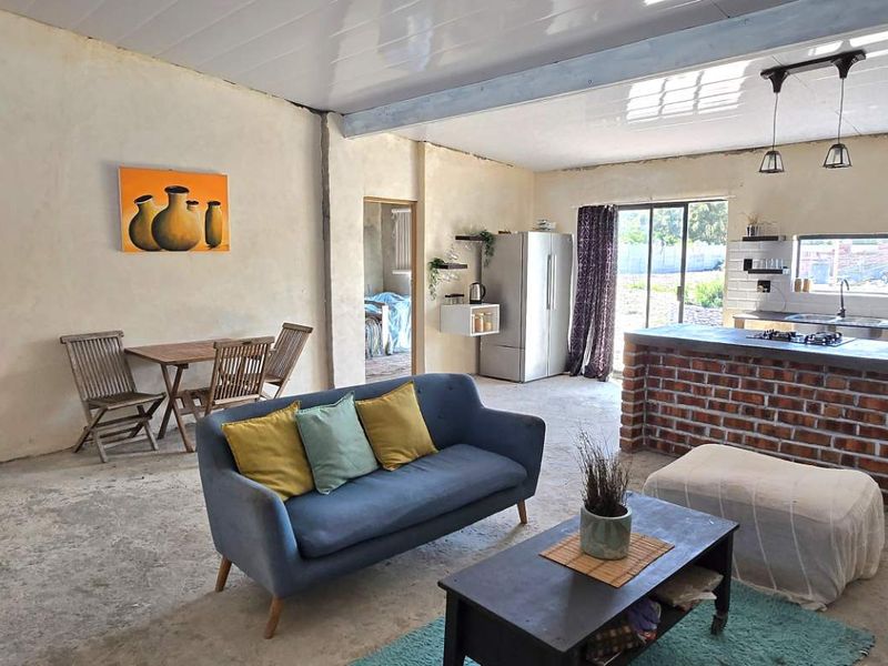 Open-plan living and kitchen area featuring an exposed brick island, subway tile backsplash, and unfinished concrete flooring, offering significant potential for renovation.