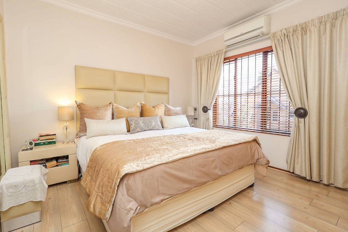 A well-maintained bedroom featuring laminate flooring, coved ceilings, and a wall-mounted air conditioning unit with wooden blinds.