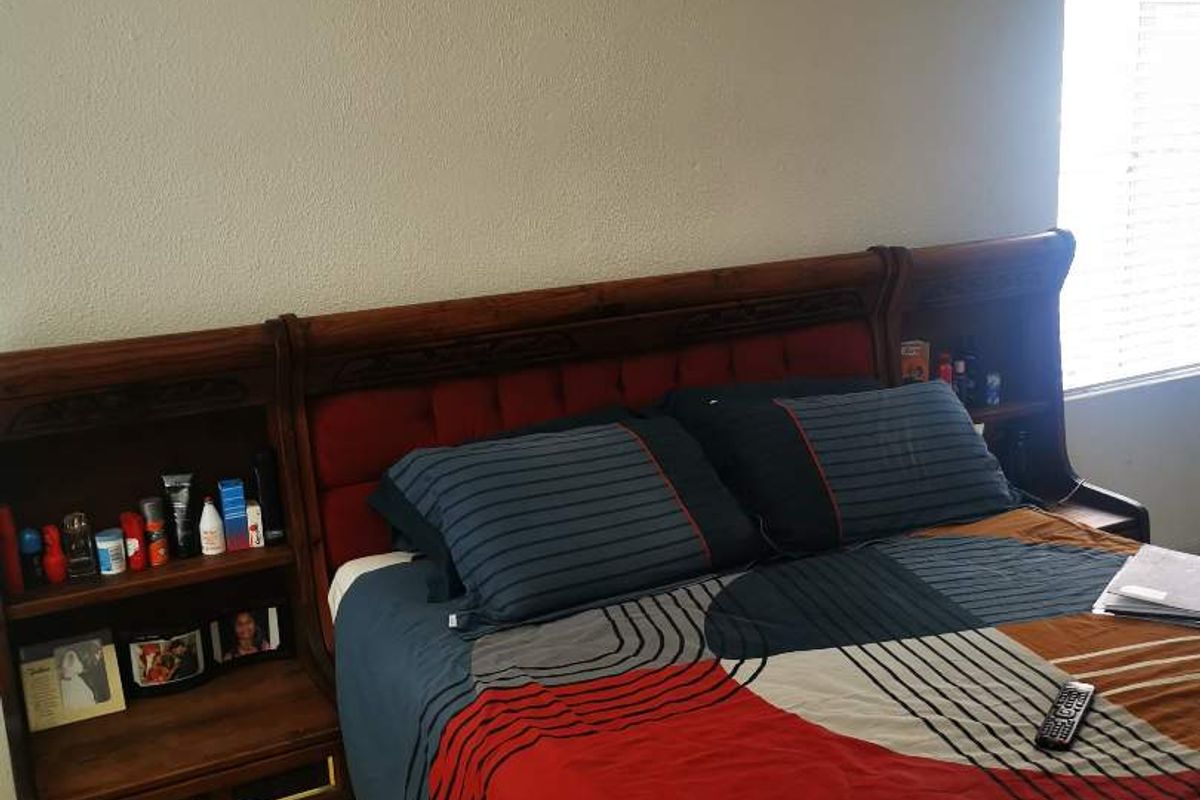 A bedroom featuring tiled flooring, a wall-mounted air conditioning unit, and a built-in wooden headboard with integrated bedside storage.