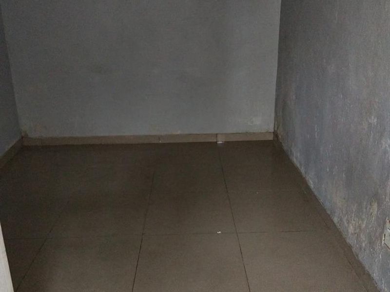 An empty, small bedroom featuring tiled flooring and plain walls showing signs of wear and surface deterioration.