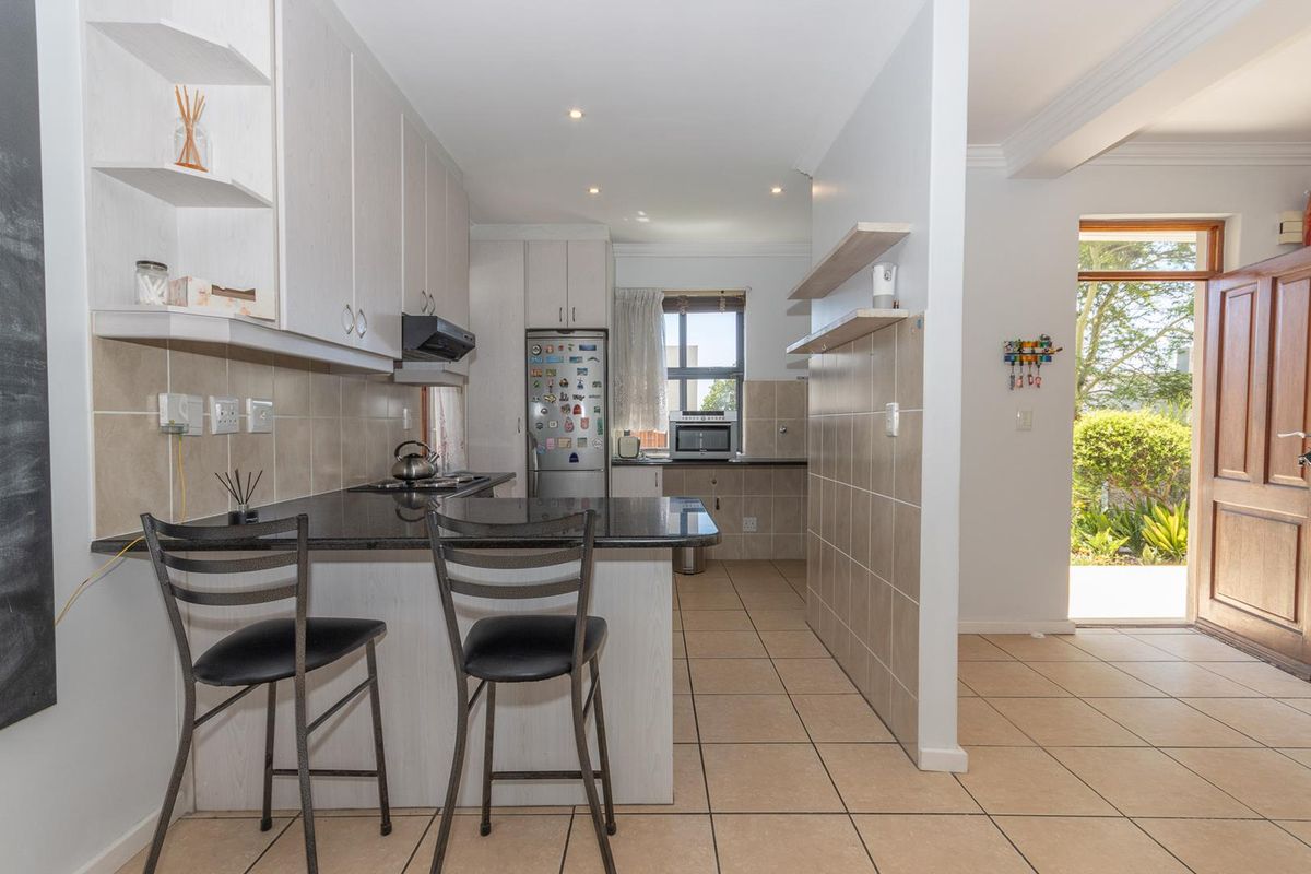 Functional kitchen featuring granite countertops, tiled backsplash, ample cabinetry, and a breakfast bar, with direct access to the home entrance.