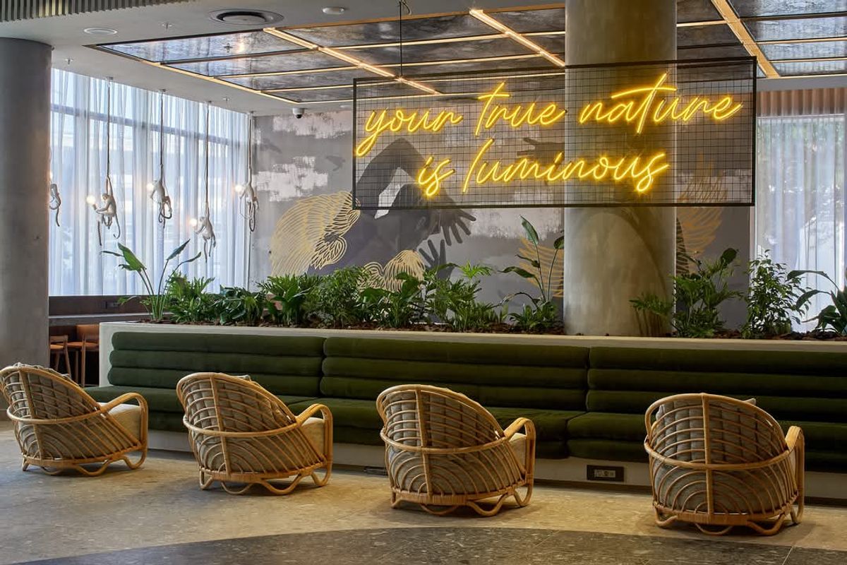A modern, stylish communal lounge area featuring built-in green velvet bench seating, decorative wall murals, and integrated ceiling lighting.
