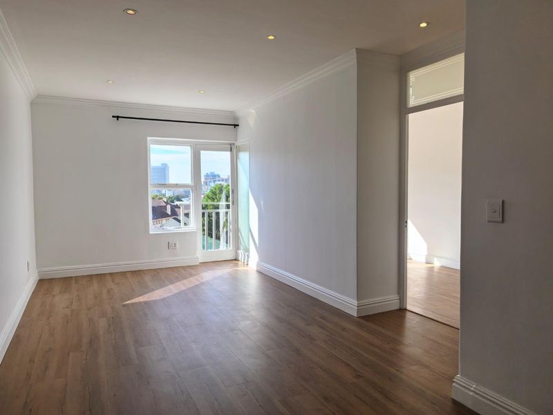 A bright, vacant living area featuring modern laminate flooring, recessed downlighting, crown molding, and access to a private balcony with city views.