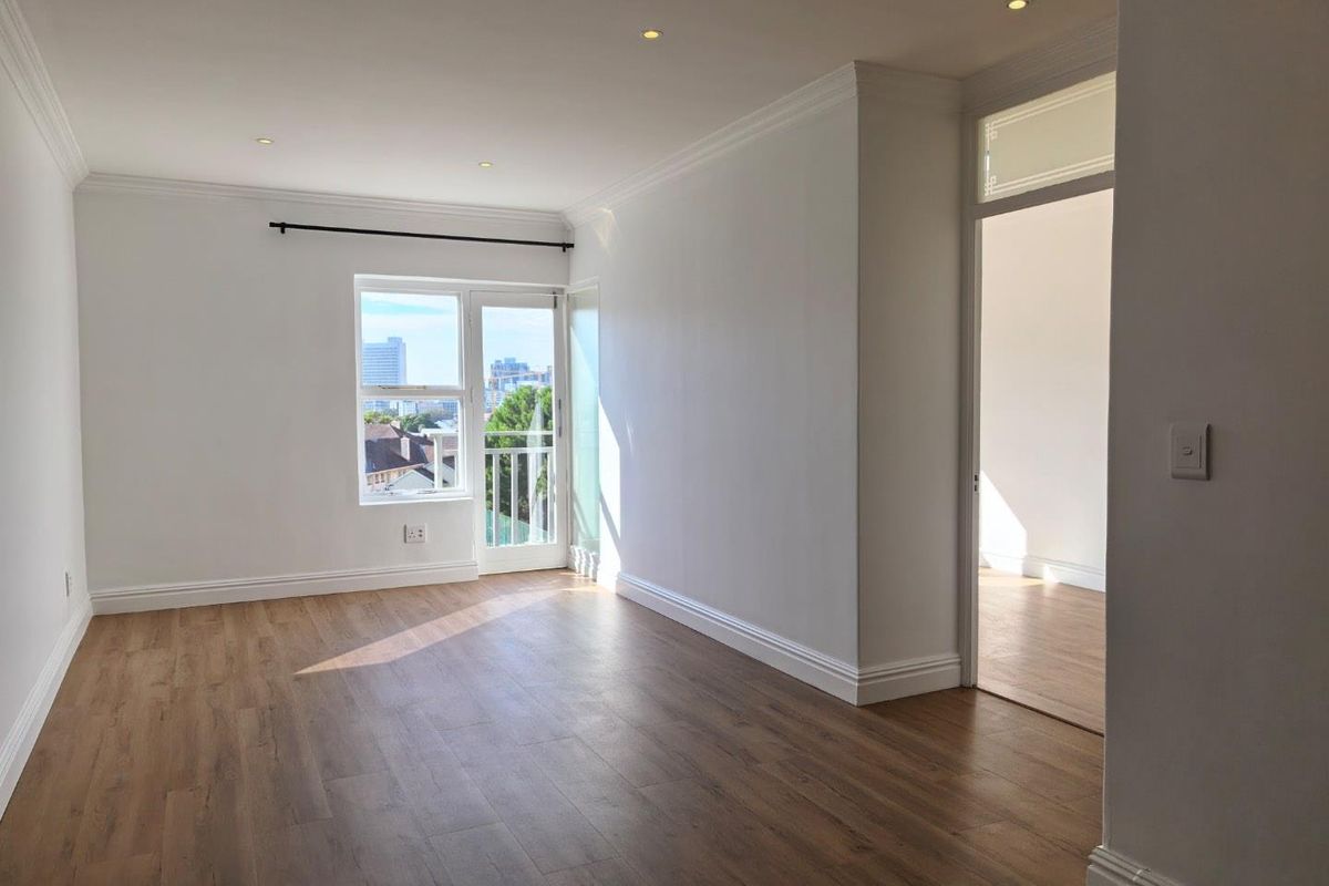 A bright, vacant living area featuring modern laminate flooring, recessed downlighting, crown molding, and access to a private balcony with city views.