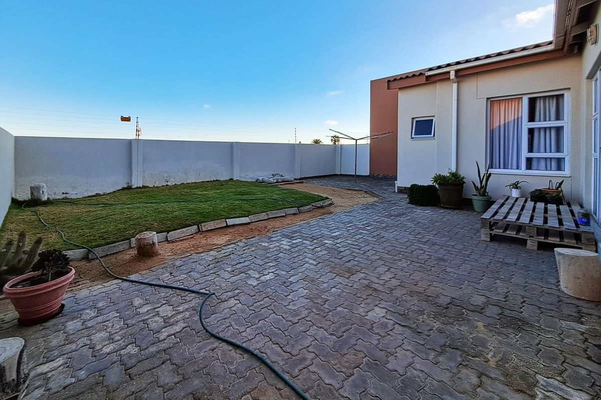 A private rear courtyard featuring paved flooring, a small lawn area, and perimeter boundary walls, offering a functional outdoor space.