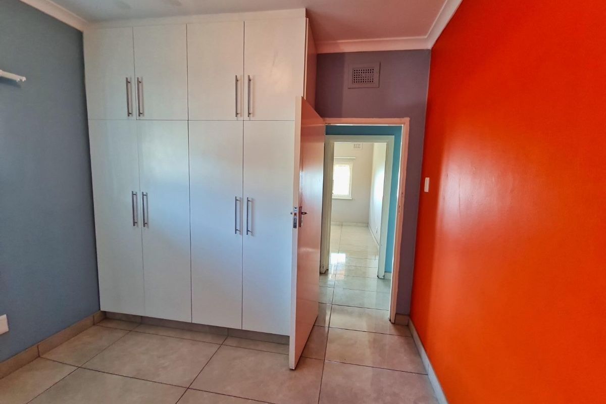 A vacant bedroom featuring built-in white cupboards, tiled flooring, and bold accent wall colors.
