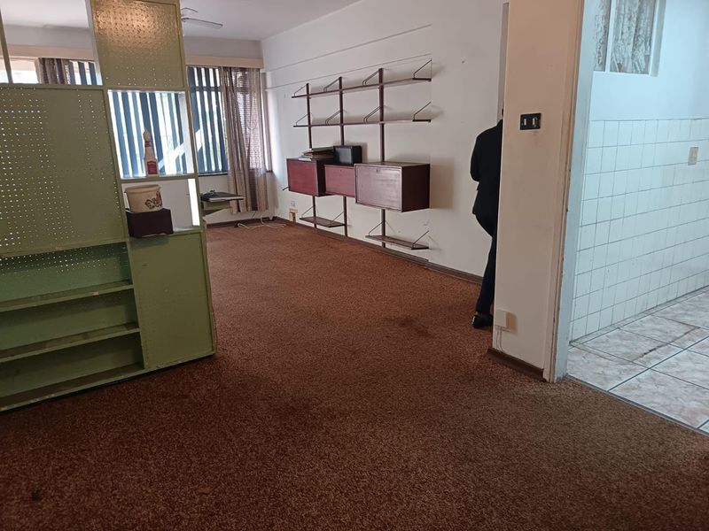 Spacious living area featuring wall-mounted shelving, carpeted flooring, and an adjacent tiled space, offering a blank canvas for modernization and renovation.
