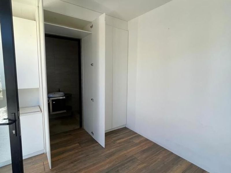 A clean, empty bedroom featuring modern laminate flooring, built-in storage cupboards, and direct access to an en-suite bathroom.