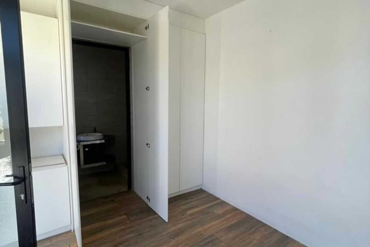 A clean, empty bedroom featuring modern laminate flooring, built-in storage cupboards, and direct access to an en-suite bathroom.