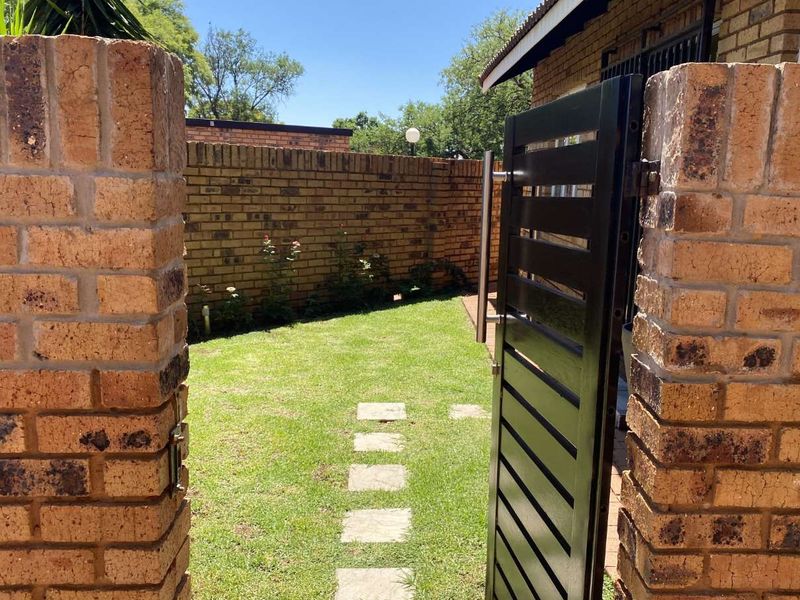 A private rear garden area featuring a well-maintained lawn, stone paver pathway, and secure brick boundary walls with a metal access gate.