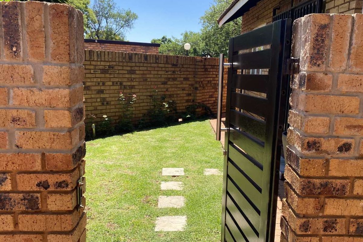 A private rear garden area featuring a well-maintained lawn, stone paver pathway, and secure brick boundary walls with a metal access gate.