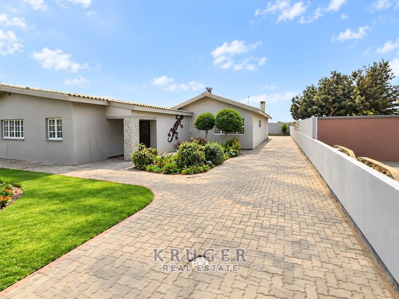 Front view of the property featuring a paved driveway, well-maintained garden, and a secure boundary wall.