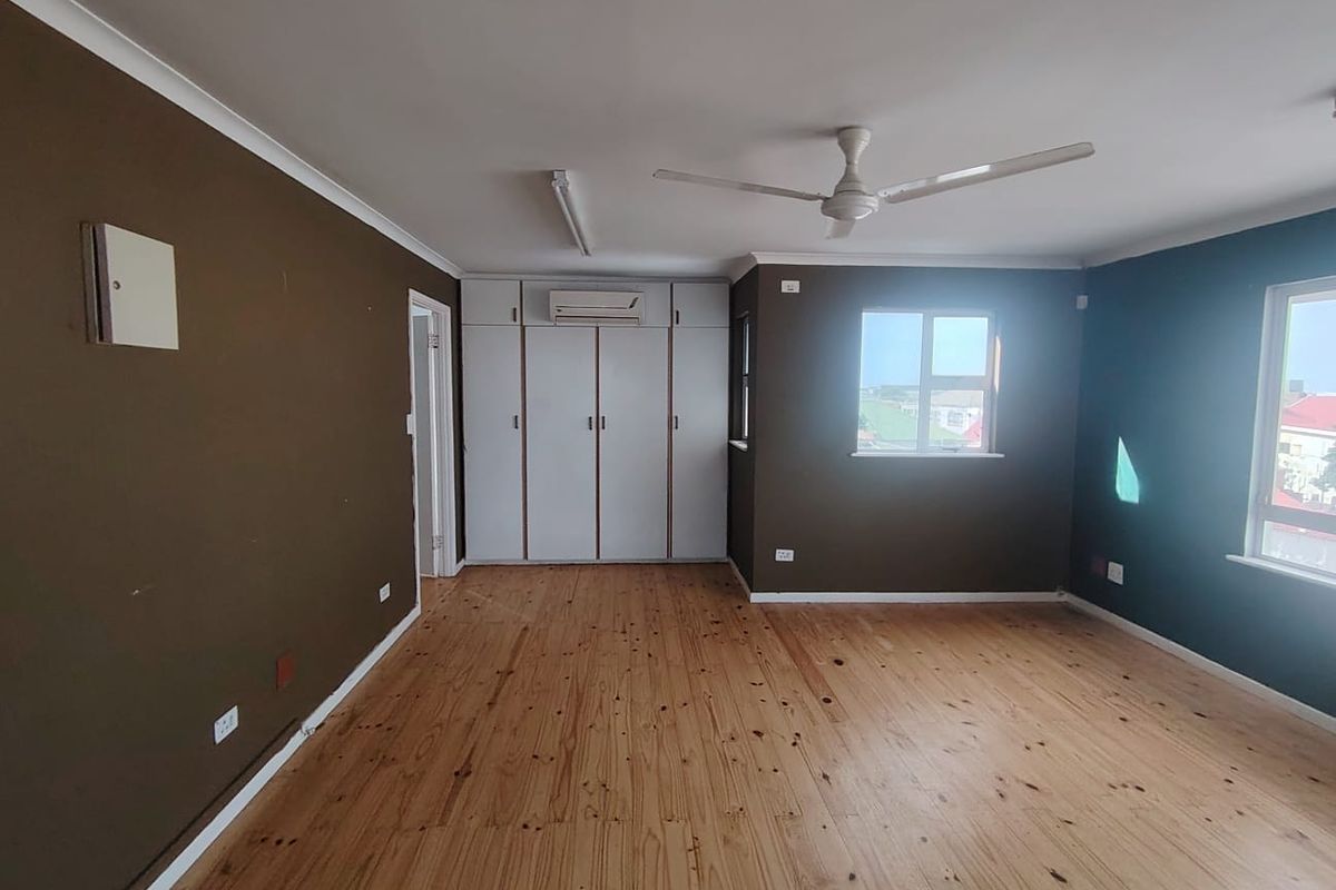 Spacious bedroom featuring polished timber flooring, built-in cupboards, a ceiling fan, and an integrated air conditioning unit.