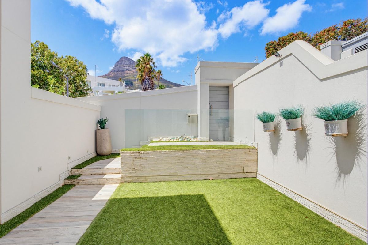 A well-maintained rear courtyard featuring artificial lawn, timber decking, stone-clad retaining wall, and a glass balustrade with mountain views.