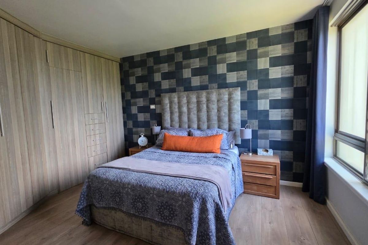 A well-maintained bedroom featuring wood-look laminate flooring, extensive built-in wardrobe storage, and a window with a security screen.