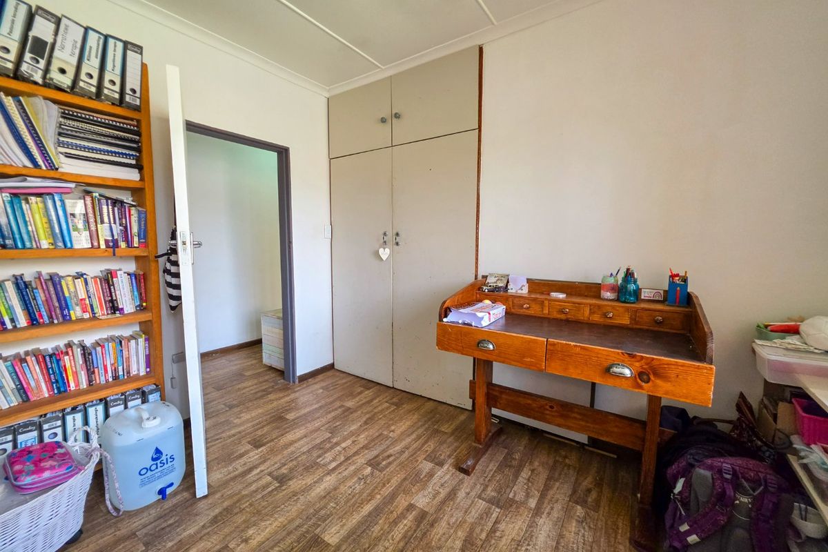 A bedroom featuring built-in cupboards and wood-look laminate flooring, providing a functional space with direct access to an adjoining room.