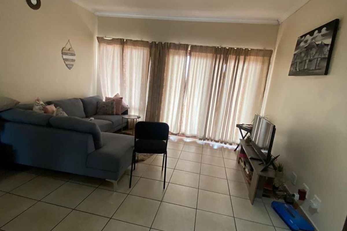 A spacious living room featuring neutral tiled flooring, recessed ceiling lighting, and large sliding glass doors that provide ample natural light.