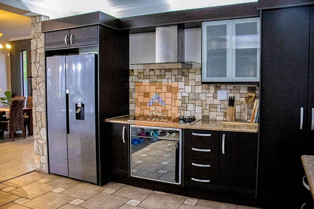 Modern kitchen featuring dark cabinetry, granite countertops, stone tile backsplash, and integrated stainless steel appliances, adjacent to an open-plan dining area.