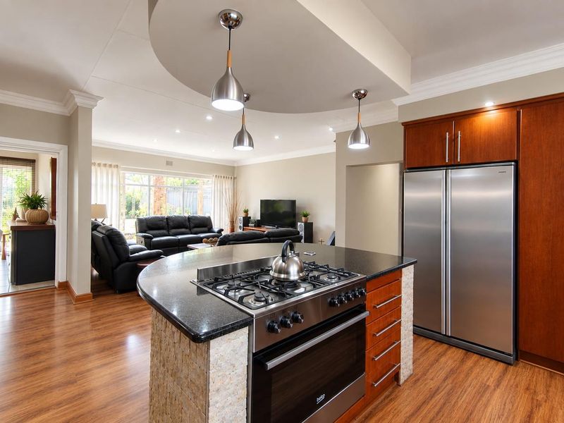Spacious open-plan kitchen and living area featuring a central island with gas cooktop, timber cabinetry, and modern pendant lighting under a recessed ceiling.