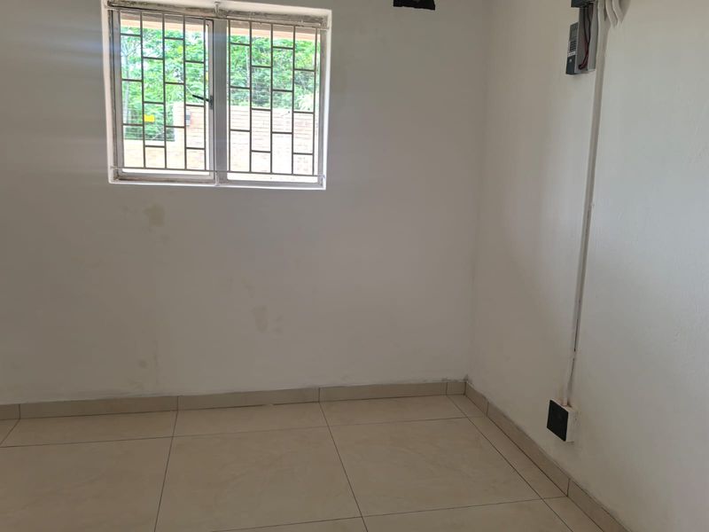An empty bedroom featuring tiled flooring, a window with security bars, and visible wall surface-mounted electrical conduit.