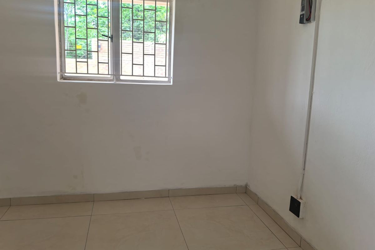 An empty bedroom featuring tiled flooring, a window with security bars, and visible wall surface-mounted electrical conduit.