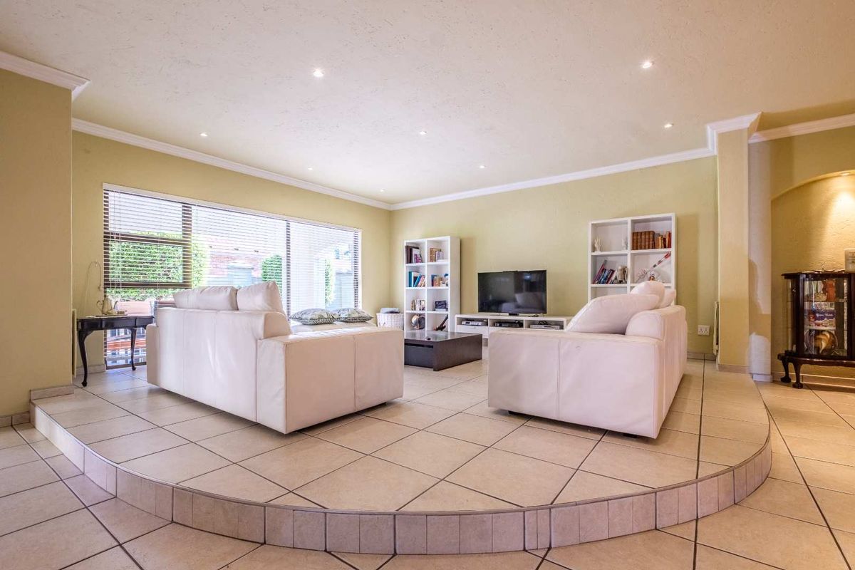 Spacious living room featuring a raised tiled platform, recessed ceiling lighting, and large windows with integrated blinds.