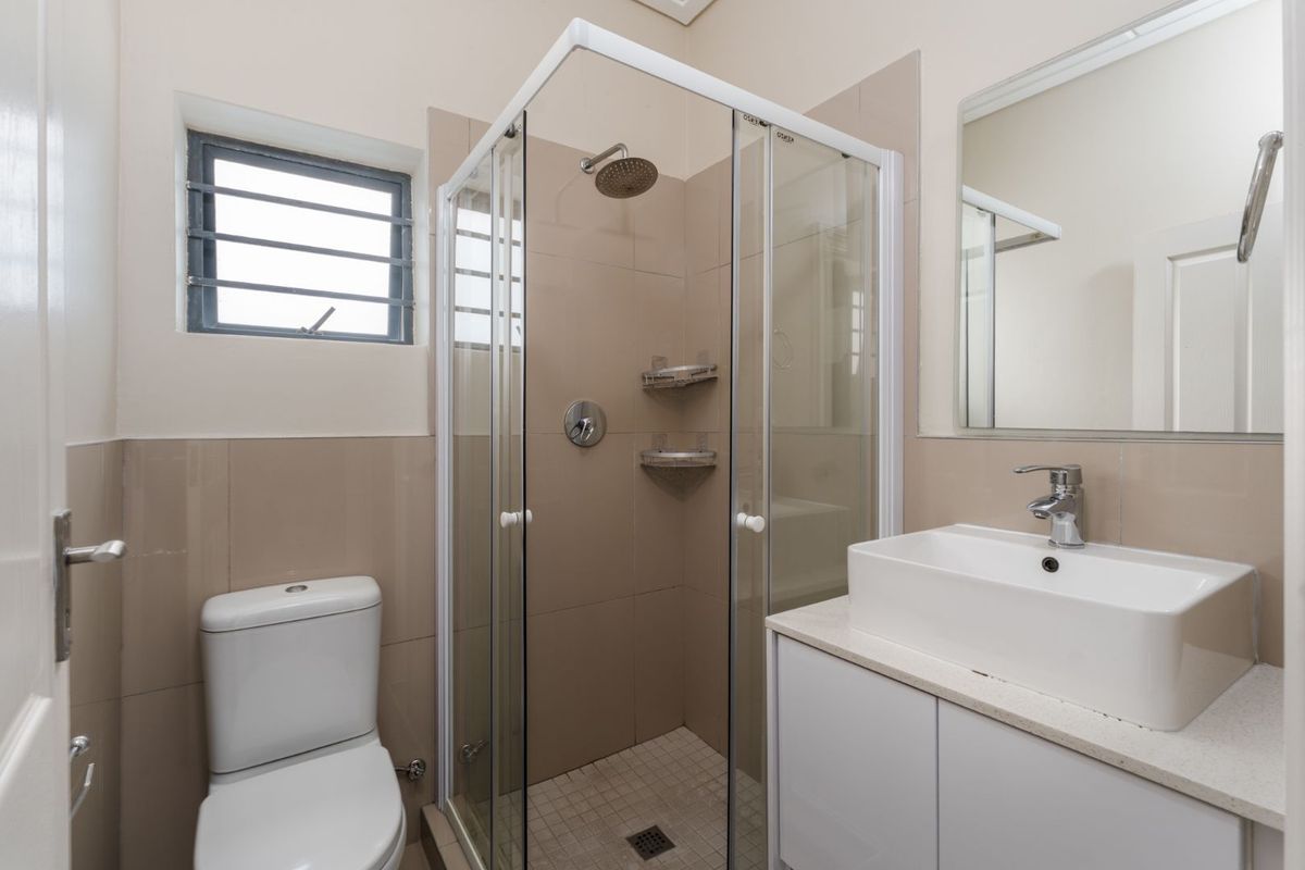 A clean, modern bathroom featuring a glass-enclosed shower, a white vanity with a basin, and neutral wall tiling.